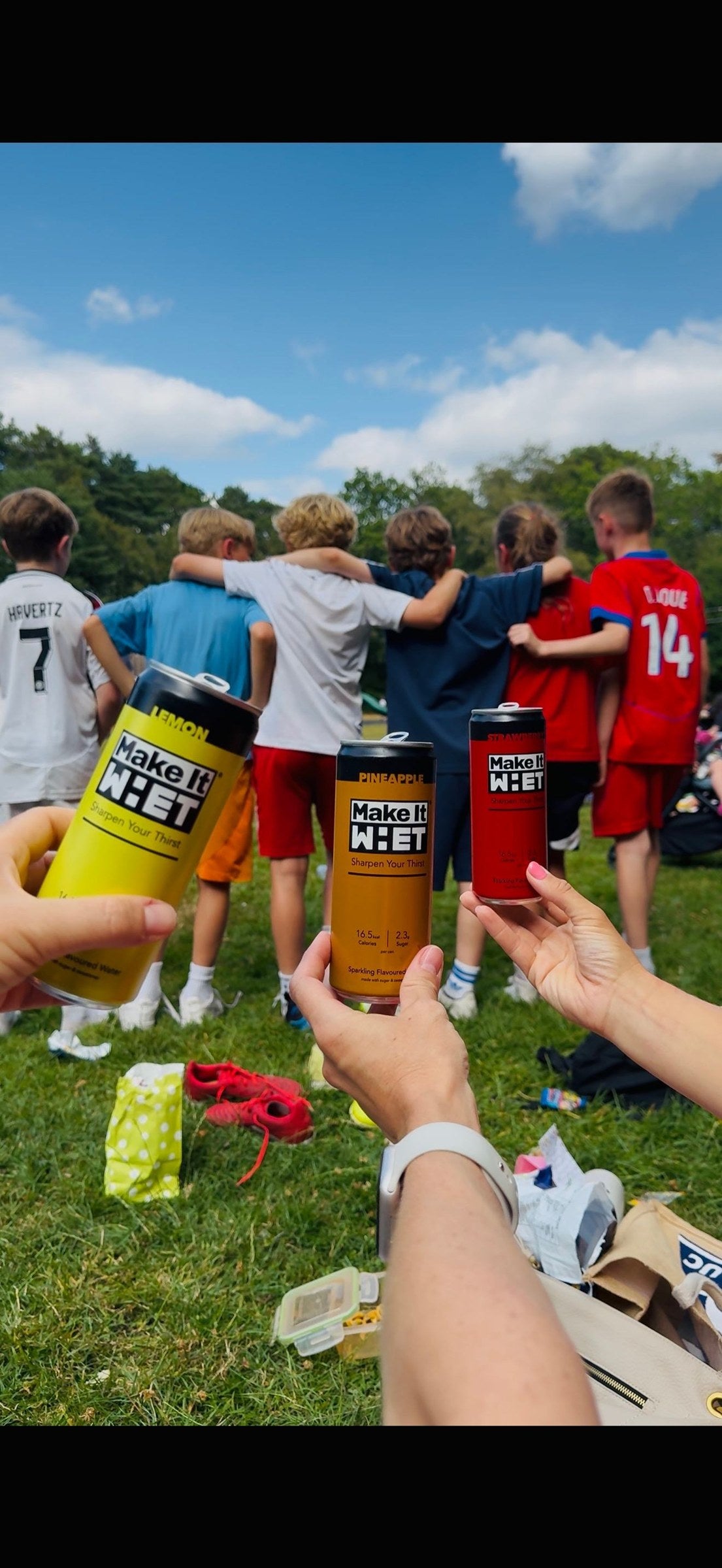 Three Make It WHET cans held together beside a sports field