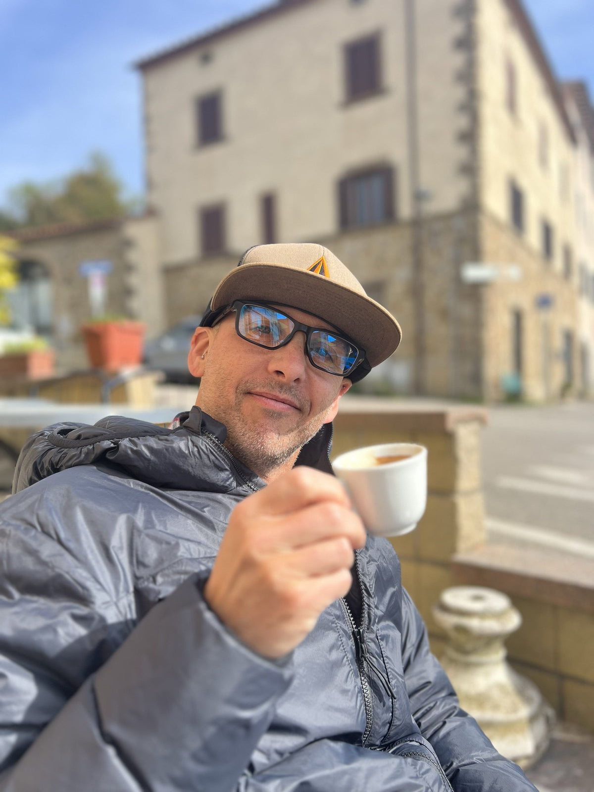 Gary wearing a cap and sunglasses and holding a coffee cup outdoors