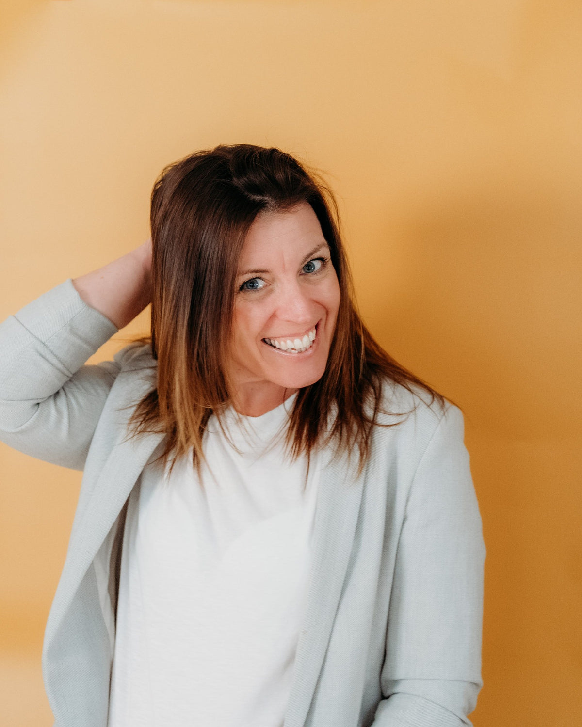 Lou smiling in a light blouse against a yellow wall