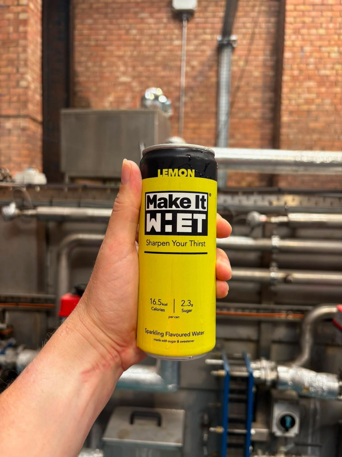 A hand holding a yellow Make It WHET can at the production site