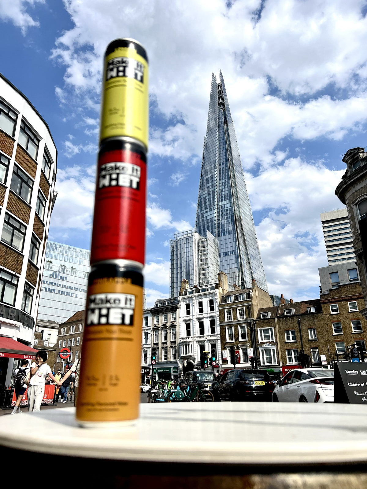 Three Make It WHET cans stacked with the Shard in the background